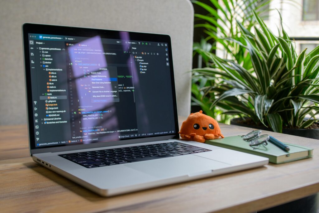 Laptop with coding interface, plant, and toy for a cozy workspace vibe.